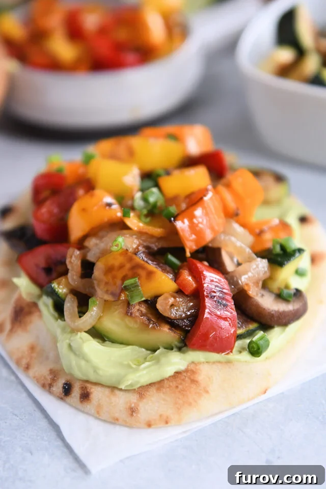 Creamy Avocado & Roasted Garden Flatbread 2 Flatbread on white parchment paper topped with creamy avocado sauce and roasted vegetables.