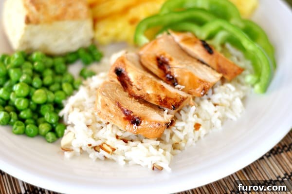 A white plate with fluffy white rice, topped with perfectly grilled teriyaki chicken strips, vibrant green pepper slices, and sweet green peas.