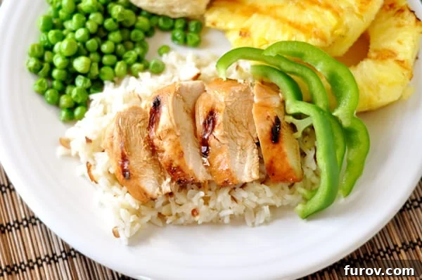 Top-down view of a beautifully arranged white plate showcasing fluffy white rice, tender teriyaki chicken slices, vibrant green pepper strips, green peas, and perfectly grilled, caramelized pineapple slices.