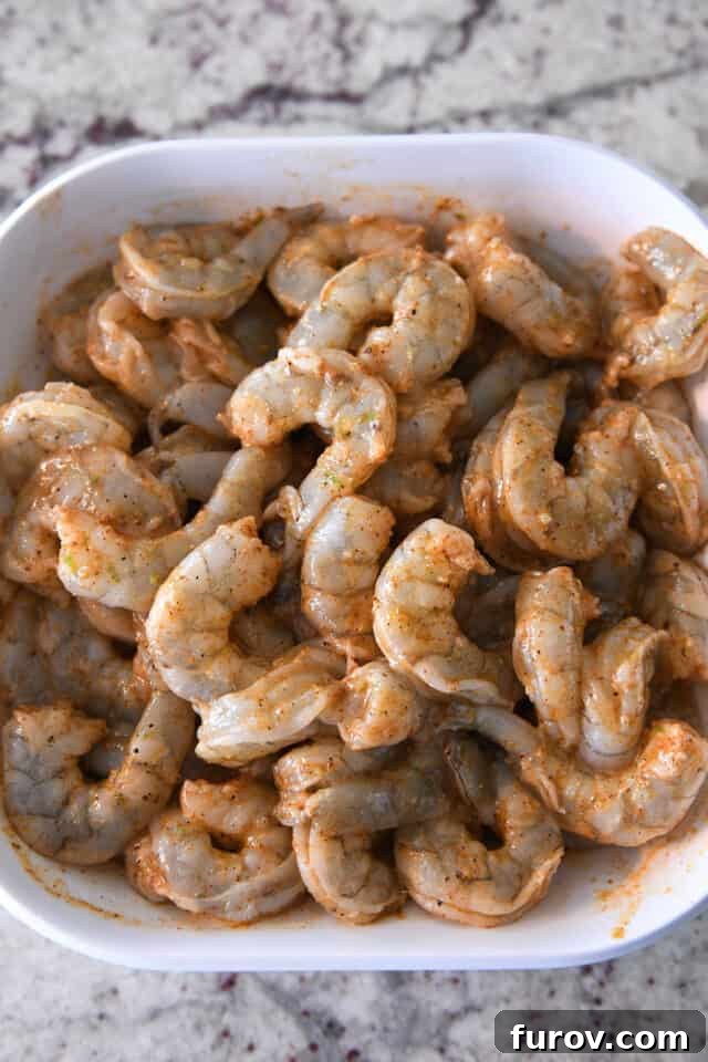 A pristine white bowl showcases a generous portion of raw shrimp, beautifully coated in a vibrant mixture of fresh lime zest and a medley of aromatic seasonings, promising an explosion of flavor.