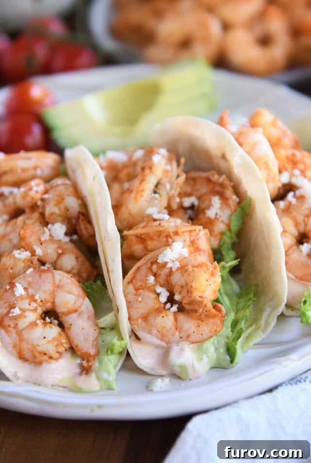 Three perfectly assembled shrimp tacos, showcasing the vibrant fillings and delicious sauces, resting invitingly on a white ridged plate.