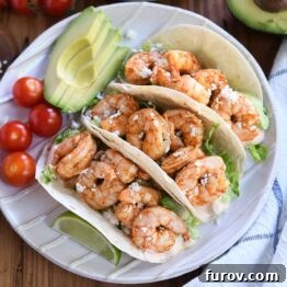 Three shrimp tacos on a white ridged plate with tomatoes and avocado, illustrating the final delicious presentation of the Easy Chile Lime Shrimp Tacos.