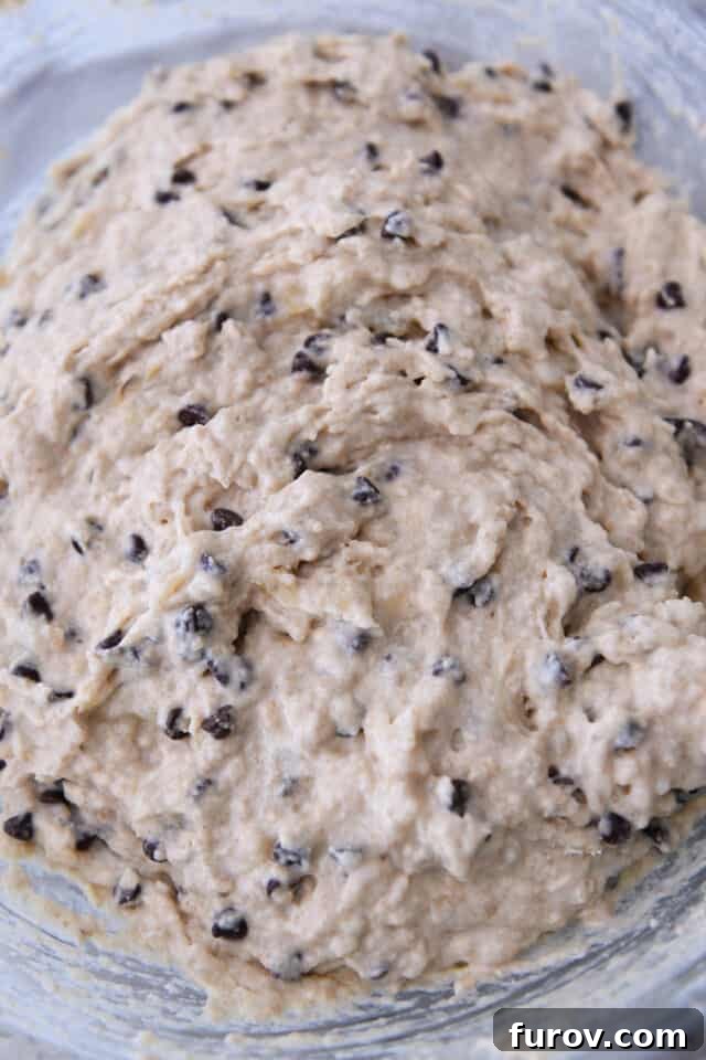 Smooth, rich banana chocolate chip muffin batter resting in a clear glass mixing bowl, ready for baking.