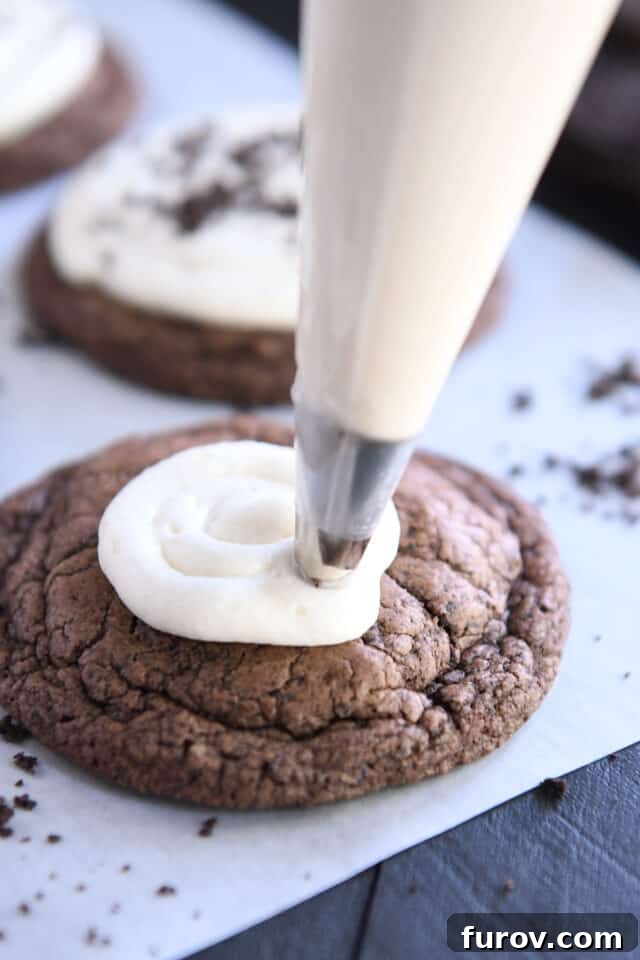 The smooth, creamy frosting being meticulously piped onto a freshly baked Chocolate Oreo Crumbl Cookie.