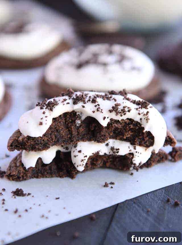 A chocolate Oreo cookie broken in half, revealing its fudgy interior, stacked on white parchment paper.