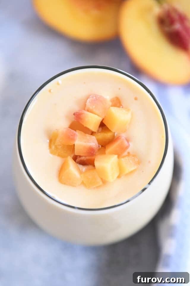 A beautiful top-down view of a sunrise peach orange protein smoothie in a glass cup, garnished with small diced peach pieces for an elegant finish.