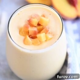 Peach orange smoothie in glass cup with diced peaches on top.