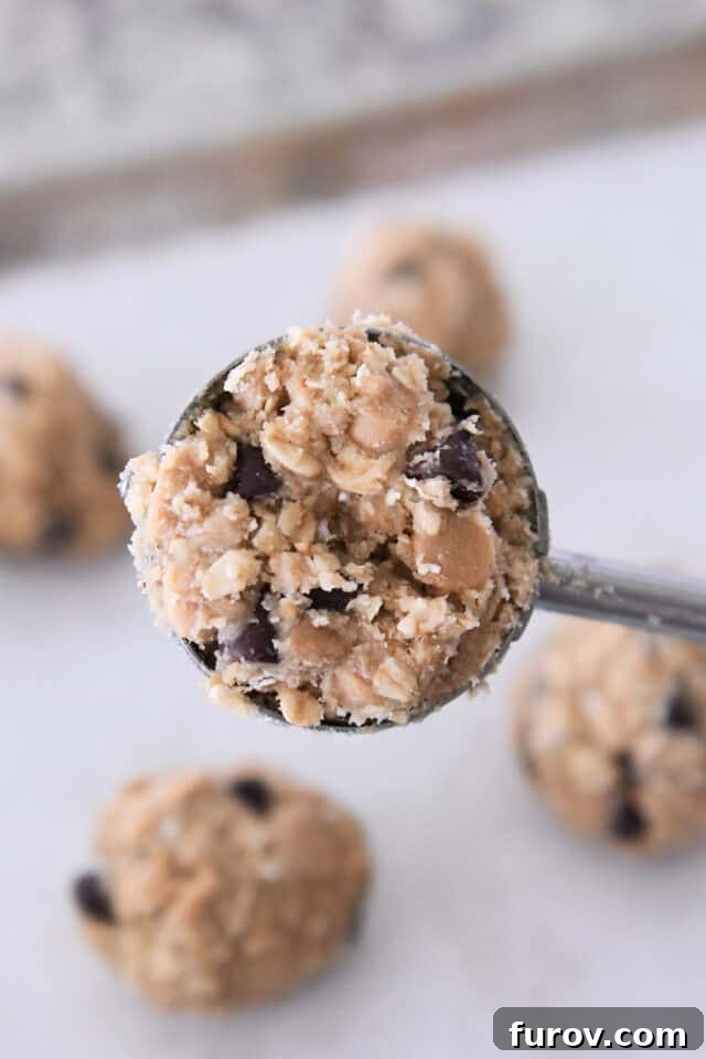 Signature Oatmeal Chocolate Chip Peanut Butter Toffee Cookies 5 A cookie scoop, filled to the brim with oatmeal chocolate chip cookie dough, visibly embedded with peanut butter chips and crunchy toffee bits.