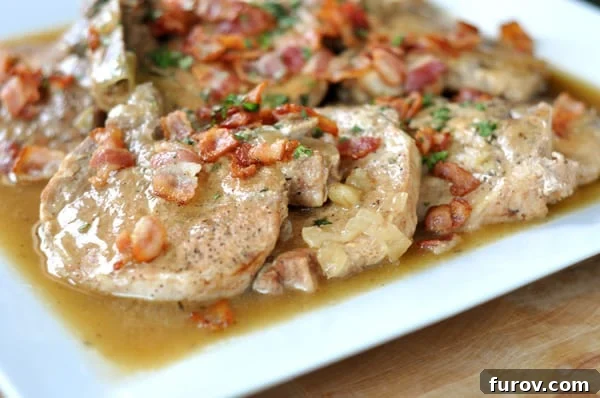 A close-up of slow cooker smothered pork chops served on a white platter, garnished with chopped fresh tomatoes and herbs, showcasing the rich gravy.