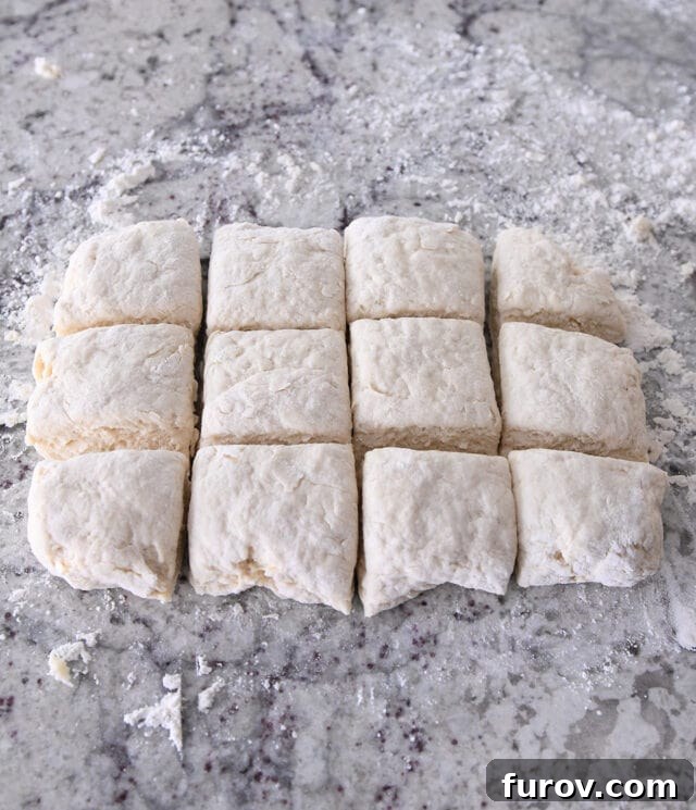 Hands carefully cutting biscuit dough into 12 even square pieces, prepared for baking.