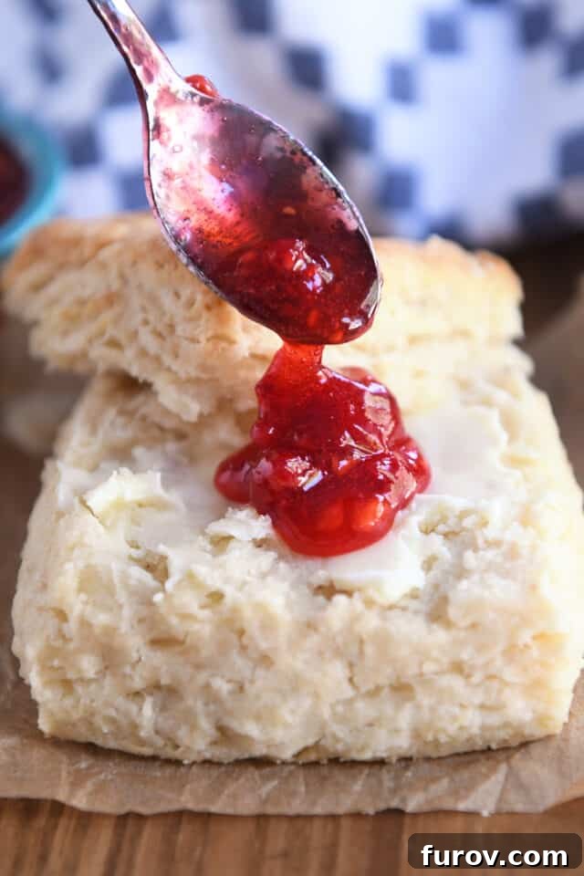 A delectable close-up of raspberry jam being dolloped generously onto a warm, buttered sourdough biscuit, ready to be enjoyed.