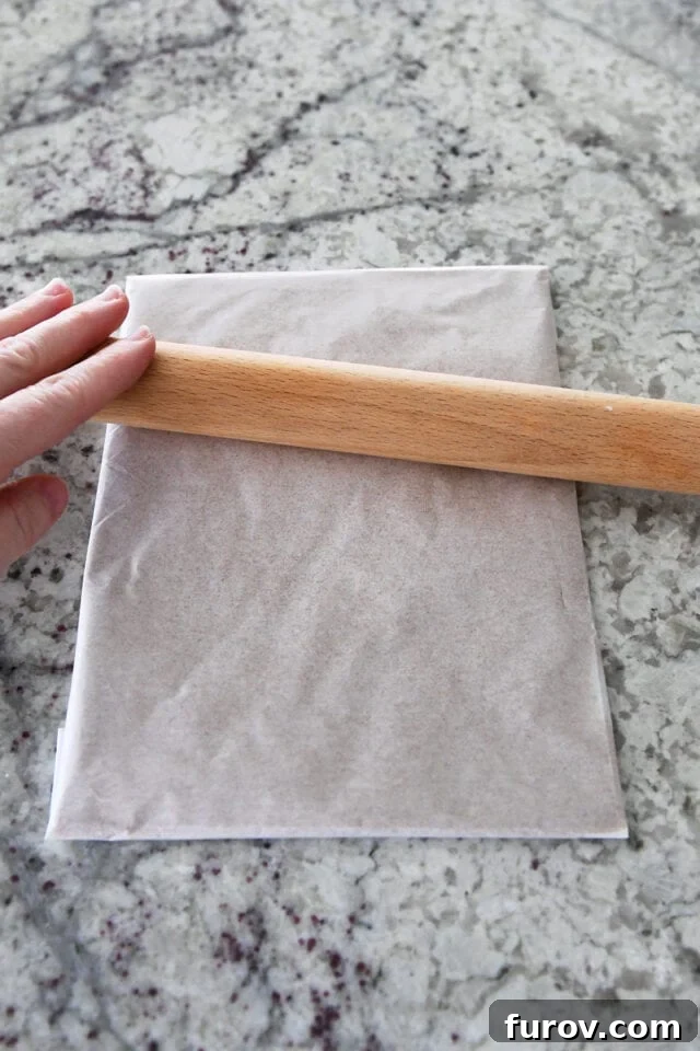 Rolling out cinnamon sugar butter packet in parchment paper with rolling pin.
