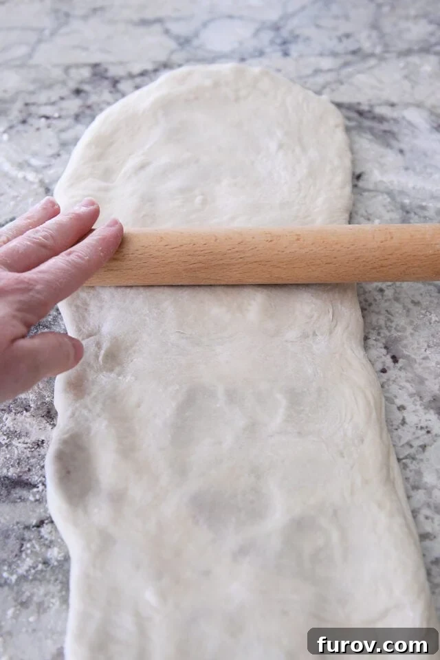 Rolling croissant bread dough into very long rectangle.