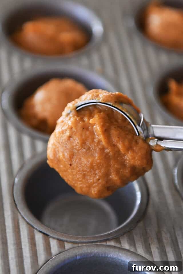 Using cookie scoop to portion pumpkin muffin batter in mini muffin tin.