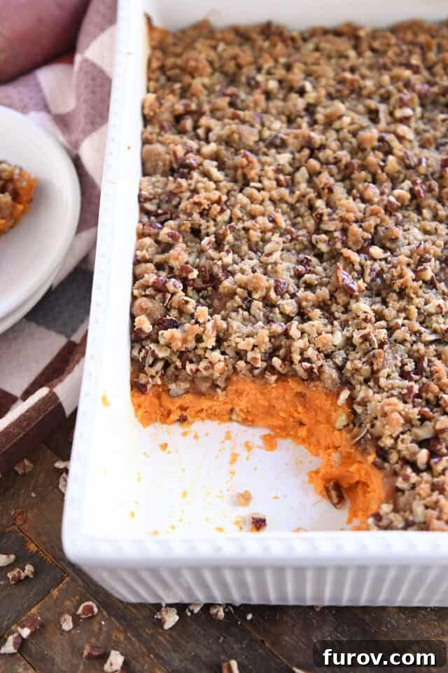 Sweet Potato Pecan Crumble Bake 2 A serving spoon lifting a scoop of creamy sweet potato casserole from a white baking dish, showcasing the golden-brown pecan topping.