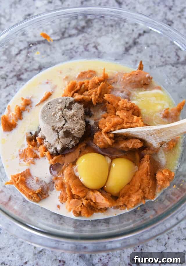 Sweet Potato Pecan Crumble Bake 3 A glass bowl containing mashed sweet potatoes alongside other ingredients like eggs, brown sugar, milk, and salt, ready for mixing.