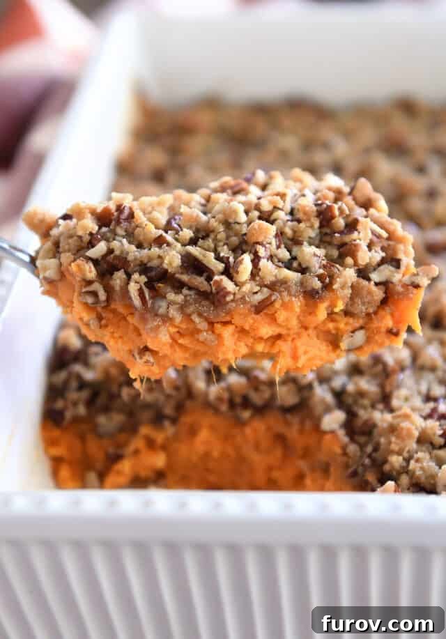 Sweet Potato Pecan Crumble Bake 7 A serving spoon lifting a generous scoop of sweet potato casserole, clearly showing the creamy filling beneath the crunchy pecan topping.