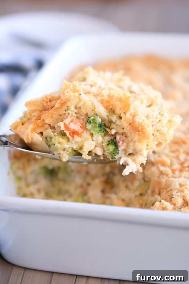 Scoop of cheesy broccoli chicken and rice casserole with buttery cracker topping on a metal serving spoon, showcasing rich texture and vibrant ingredients.