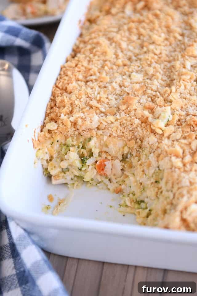 A scoop taken out of a white casserole pan, revealing the creamy, cheesy broccoli chicken and rice casserole inside.