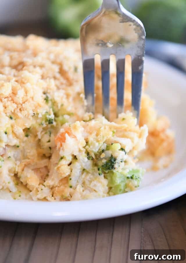 A fork taking a bite of the cheesy broccoli chicken and rice casserole, showcasing the texture of rice, broccoli, and carrots.