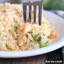Fork scooping bite of casserole on white plate with rice, broccoli and carrots.