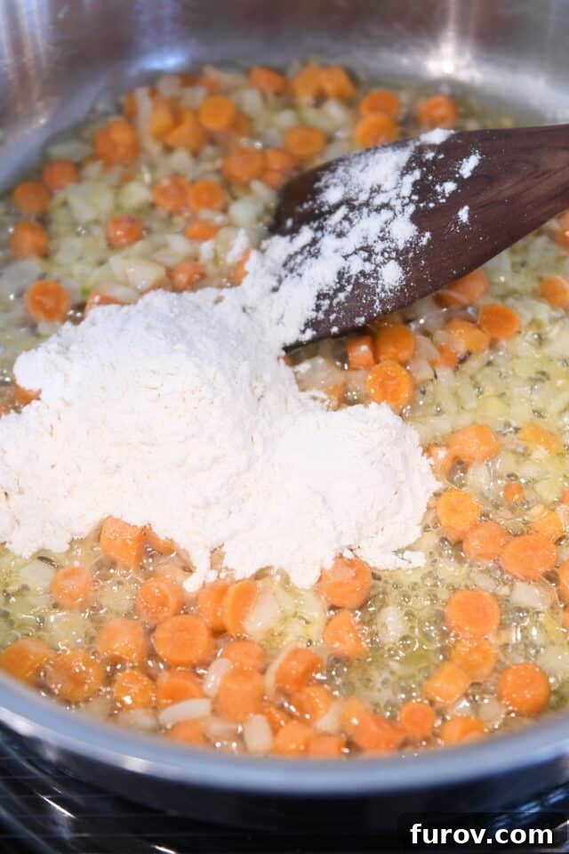 Adding flour to a skillet with melted butter and sautéed carrots, onions, and garlic to create a roux for the cheese sauce.