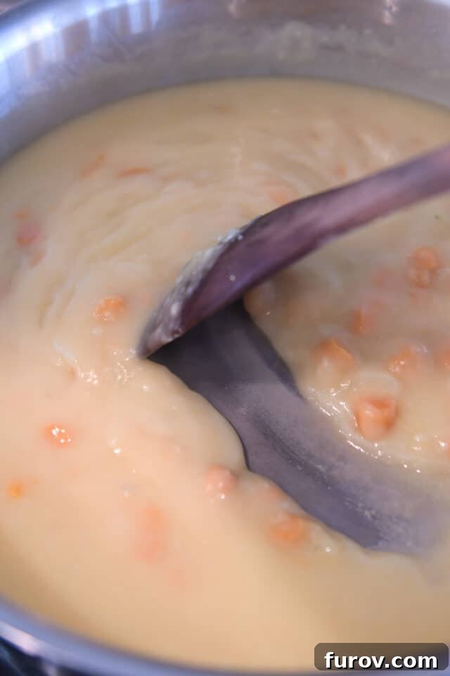 Thick, creamy cheese sauce with diced carrots simmering in a skillet, ready for other ingredients.