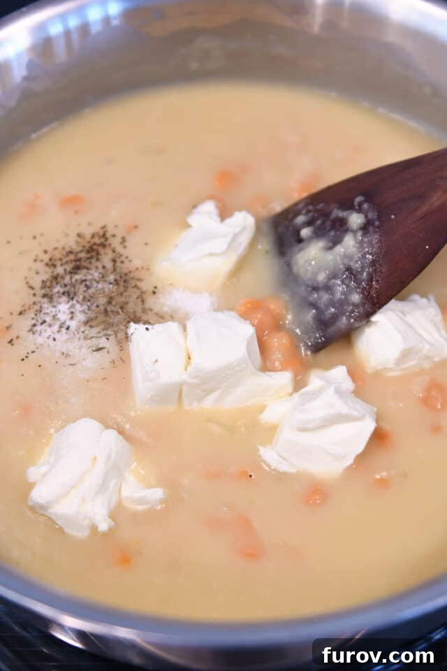 Adding softened cream cheese, salt, pepper, and thyme to the simmering cream sauce in a skillet with carrots.