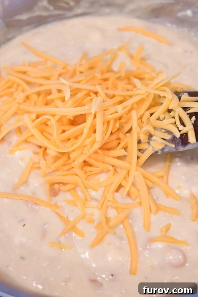 Stirring freshly shredded cheddar cheese into the rich, creamy sauce in a skillet, ensuring it melts smoothly.