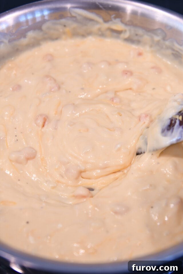 Stirring the creamy, cheesy sauce with a wooden spoon in a skillet, ensuring all ingredients are well combined.