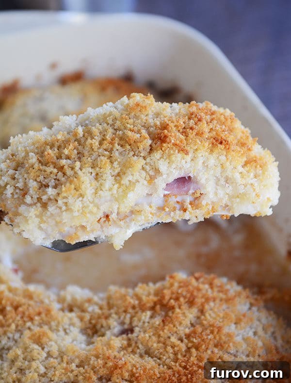 A golden-brown, breaded chicken cordon bleu casserole portion being lifted from a baking dish, showcasing its cheesy interior.