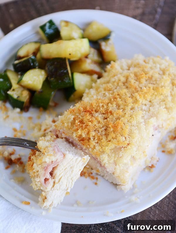 A plated easy chicken cordon bleu portion, with a bite taken, served alongside sautéed zucchini for a balanced meal.