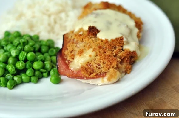 A beautifully plated easy chicken cordon bleu, covered in creamy sauce, served with peas and roasted potatoes.