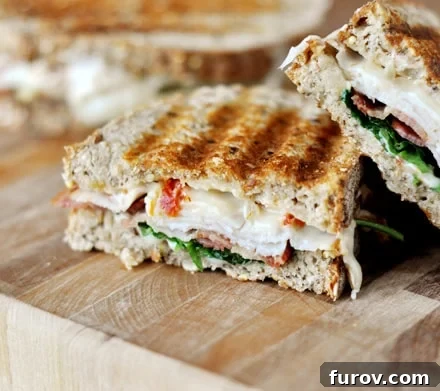 Gourmet Smoked Turkey Club Panini 3 A smoked turkey club panini, sliced in half diagonally, with one half slightly angled on top of the other, showcasing the vibrant ingredients and melted cheese.