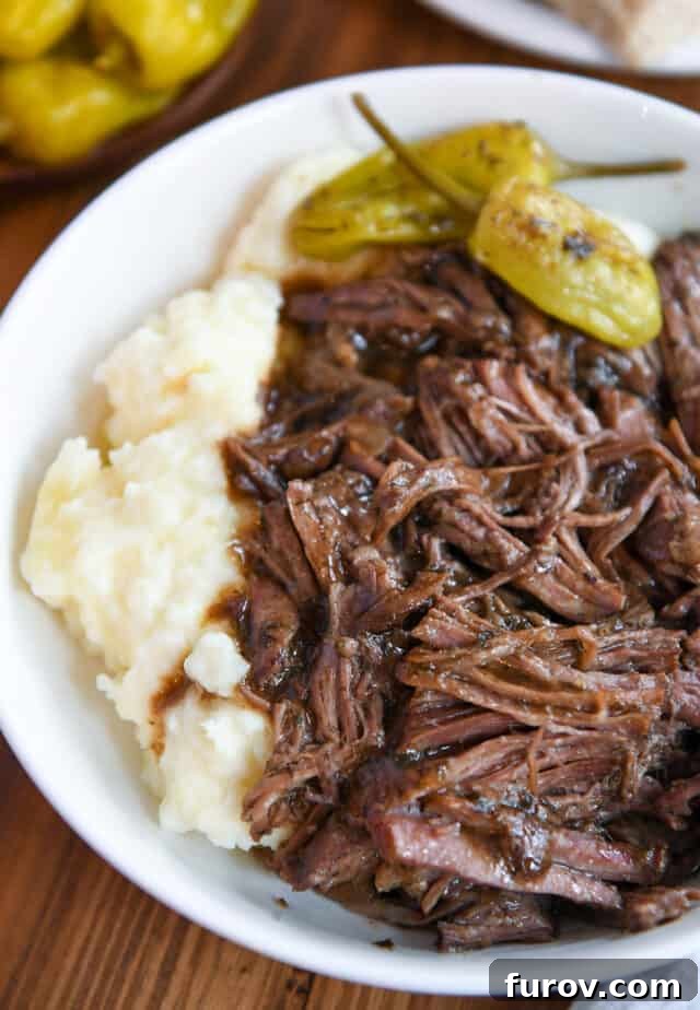White bowl with mashed potatoes, shredded beef and gravy, and pepperoncini.