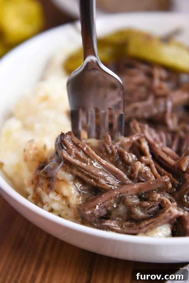 Fork taking bite of mashed potatoes, shredded beef and gravy.