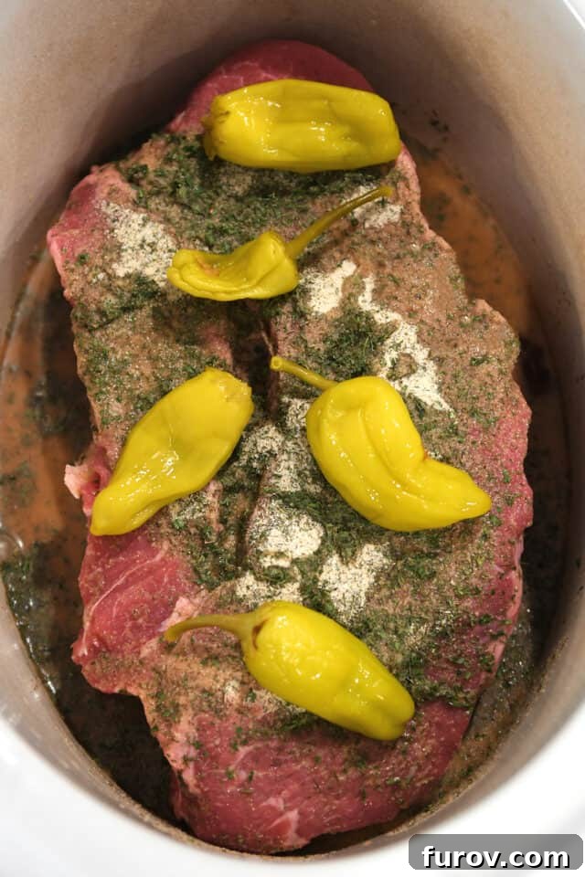 Chuck roast in slow cooker insert with pepperoncini, seasonings and beef broth.