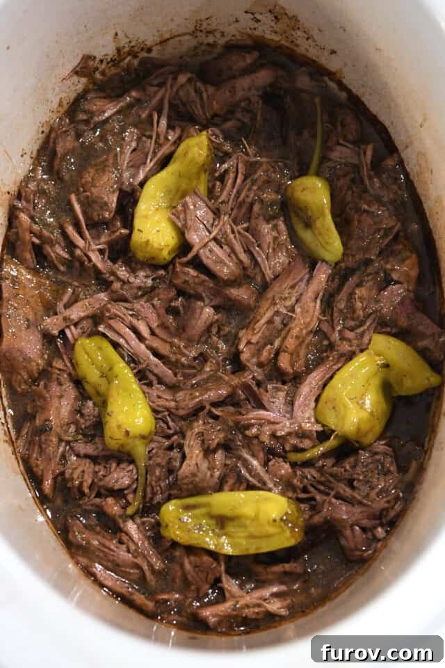 Shredded beef in slow cooker with gravy and pepperoncini.