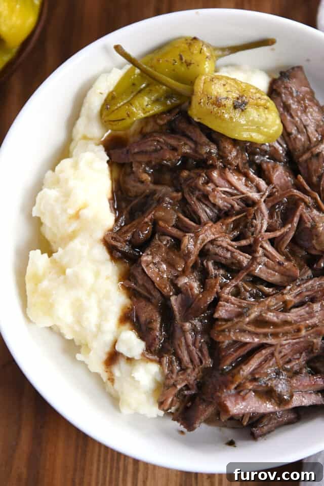 Top down view of white shallow bowl with mashed potatoes, shredded beef and gravy, and two pepperoncini.
