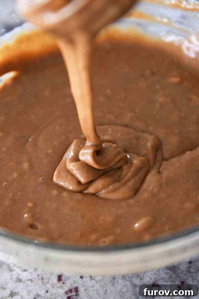 Thick gingerbread batter drizzling into a bowl from a whisk, showing perfect consistency.