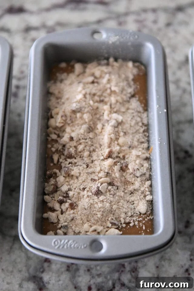 Mini loaf pan filled with gingerbread batter, topped with a generous sprinkle of streusel before baking.