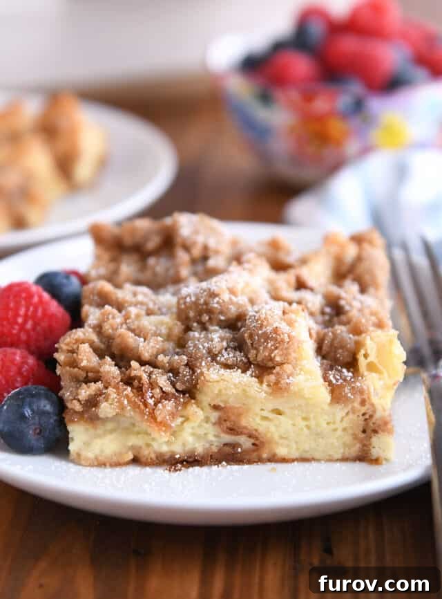 Cinnamon Streusel French Toast Casserole 2 Square serving of French toast bake on white plate with fresh berries and powdered sugar.