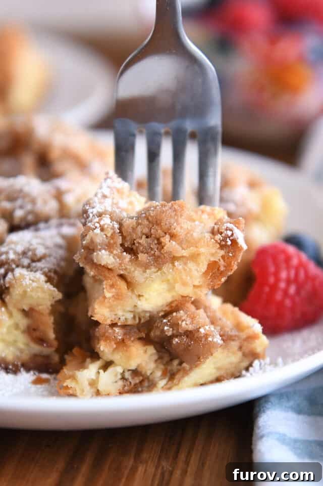 Cinnamon Streusel French Toast Casserole 9 Fork skewering two bites of baked French toast on white plate.