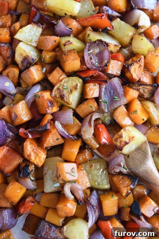 A vibrant mix of roasted potatoes, red onions, red bell peppers, and butternut squash arranged on a baking sheet, showcasing their golden-brown edges and tender texture.