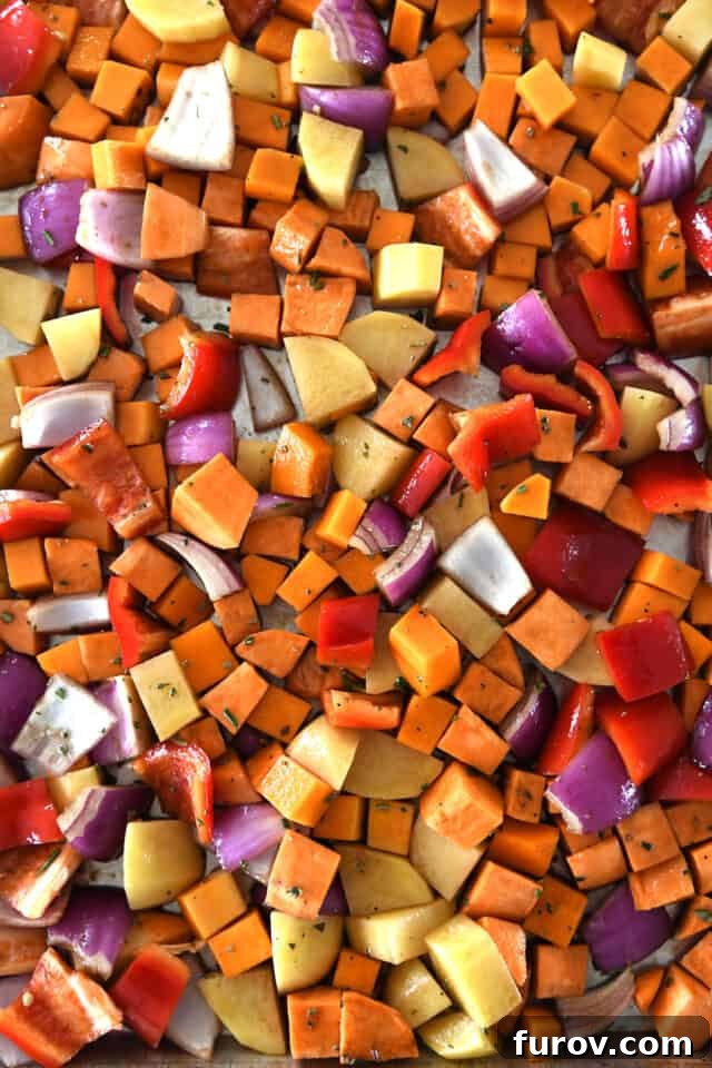 A sheet pan with uncooked winter vegetables generously drizzled with the balsamic vinaigrette, showing the readiness for roasting.