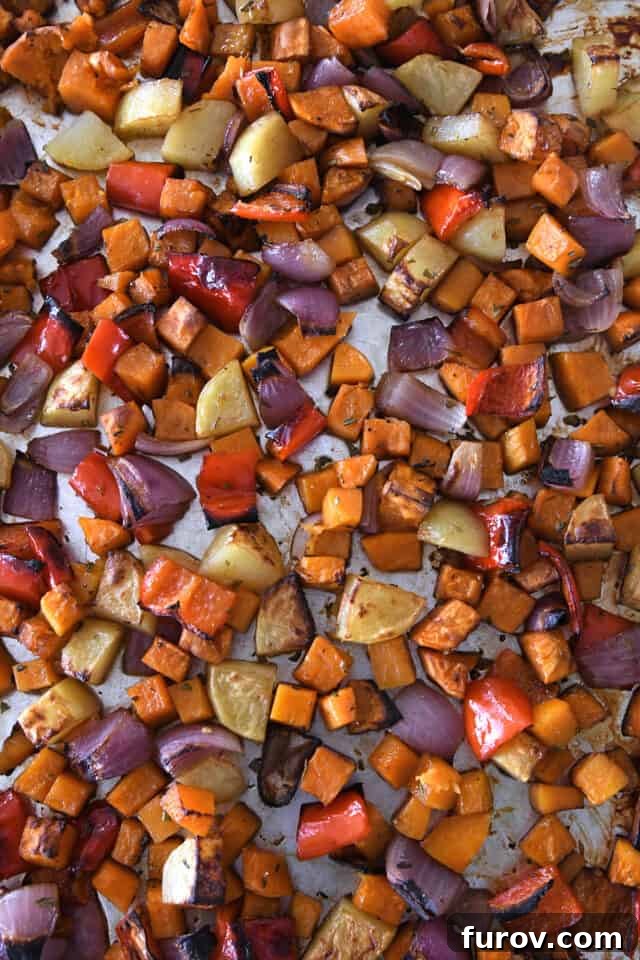A close-up view of cooked and perfectly roasted winter vegetables on a sheet pan, showcasing their caramelized surfaces and tender appearance.