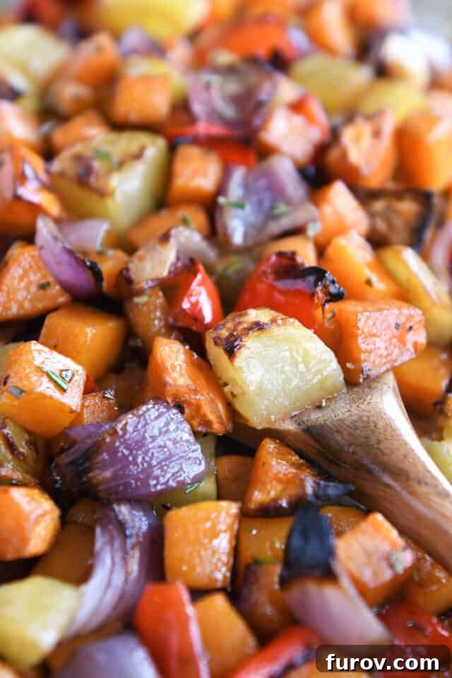 A close-up of a sheet pan filled with golden-brown roasted potatoes, red onions, red bell peppers, and butternut squash, ready to be served.