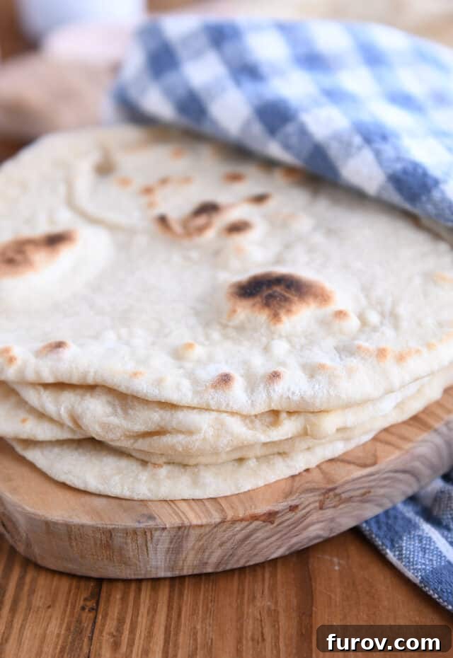 Stack of four sourdough flatbreads on wood cutting board, showcasing their golden brown spots and soft texture.