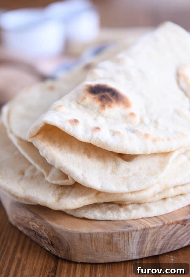 A folded sourdough flatbread resting on a stack of other flatbreads on a wooden cutting board.