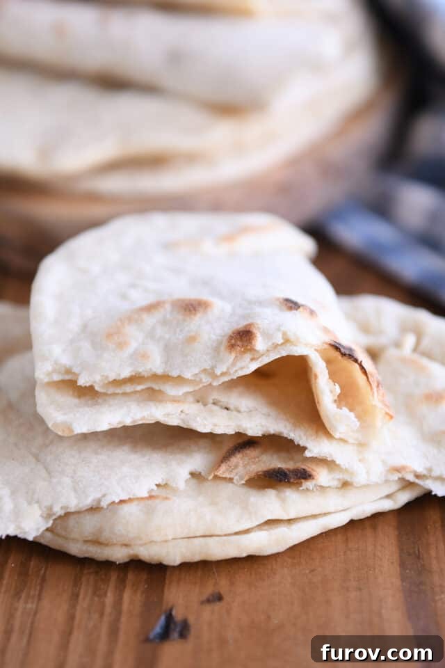 A ripped piece of sourdough flatbread revealing its airy interior, resting on two other pieces.